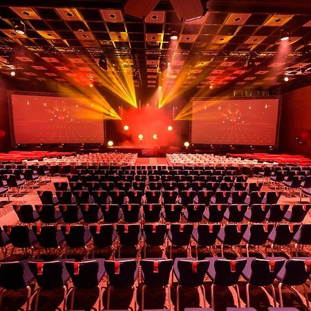 Crowne Plaza Moscow World Trade Centre, An Ihg Hotel Eksteriør billede The photo shows a spacious event hall set up for an audience. There are numerous rows of blue chairs arranged facing two large screens at the front. The room is illuminated by dynamic lighting effects, with beams of light projecting from various angl